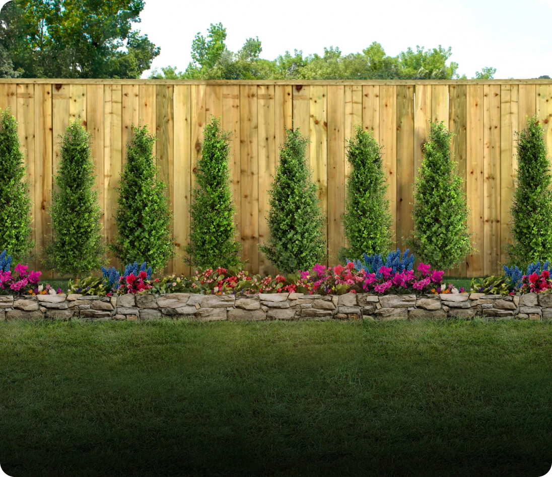 Trees and flowers in front of wooden fence.